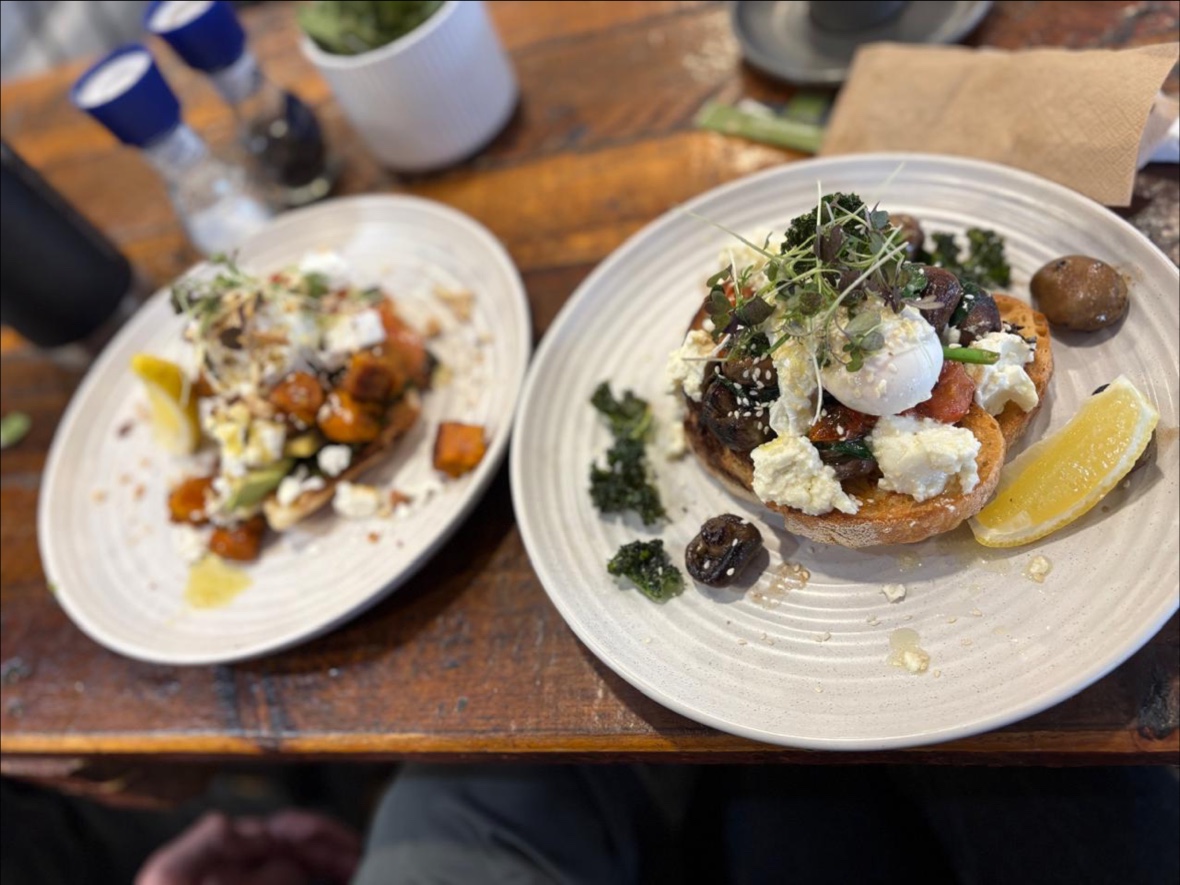 Two brunch plates with poached eggs, mushrooms, roast pumpkin and feta on a timber table